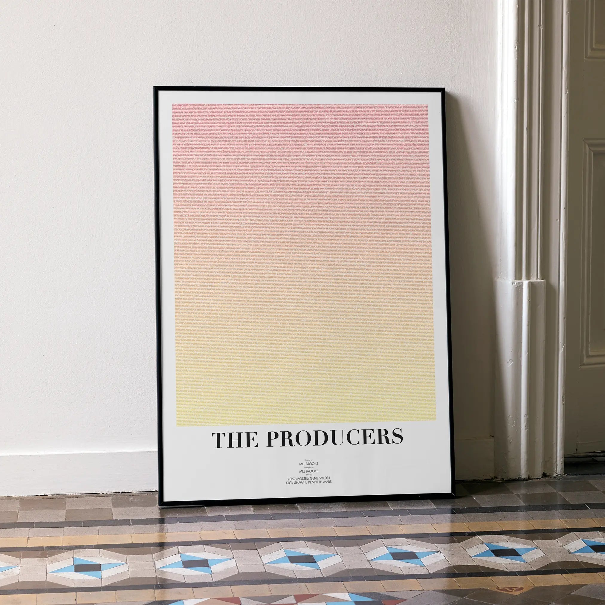 A framed The Producers movie script poster leaning against a wall in a minimalist interior.
