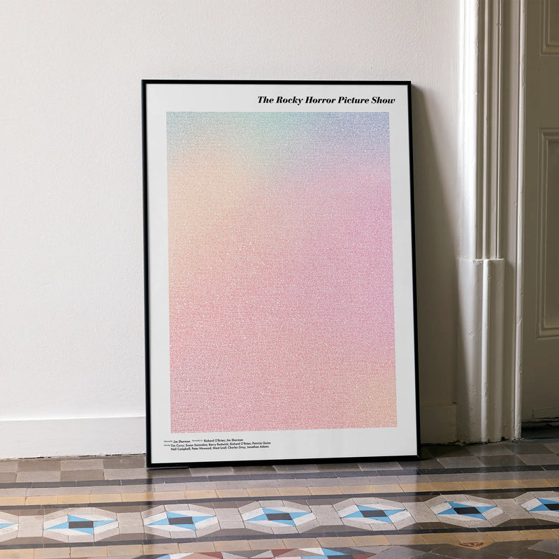 A framed The Rocky Horror Picture Show movie script poster leaning against a wall in a minimalist interior.