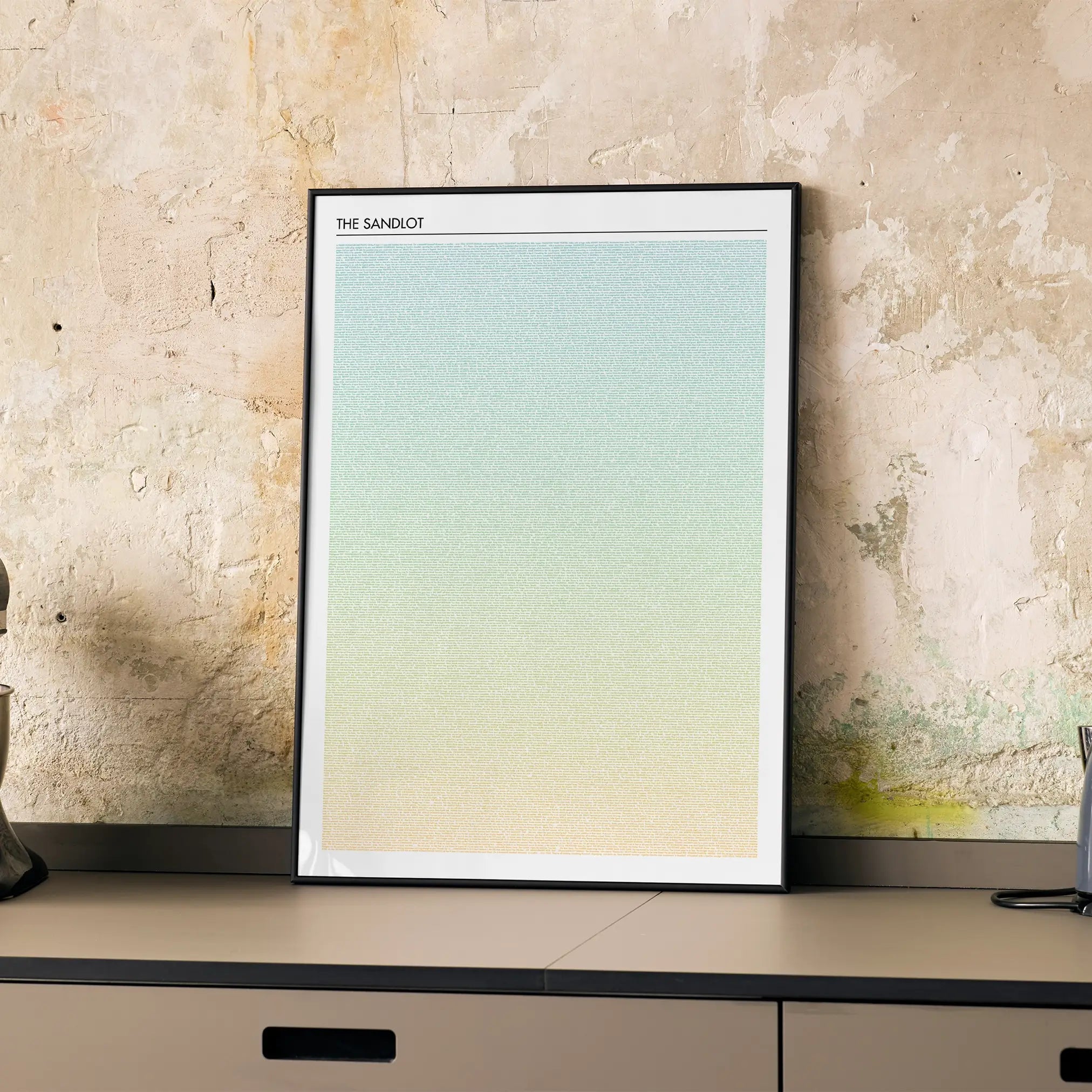 A framed The Sandlot movie script poster displayed on a cabinet in a minimalist interior.