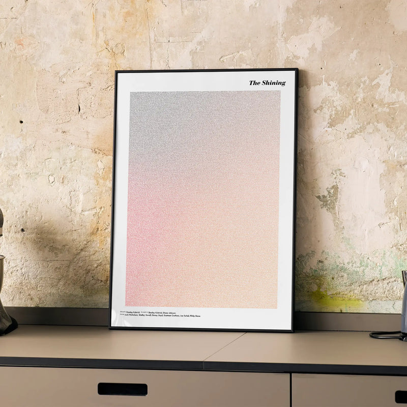 A framed The Shining movie script poster displayed on a cabinet in a minimalist interior.