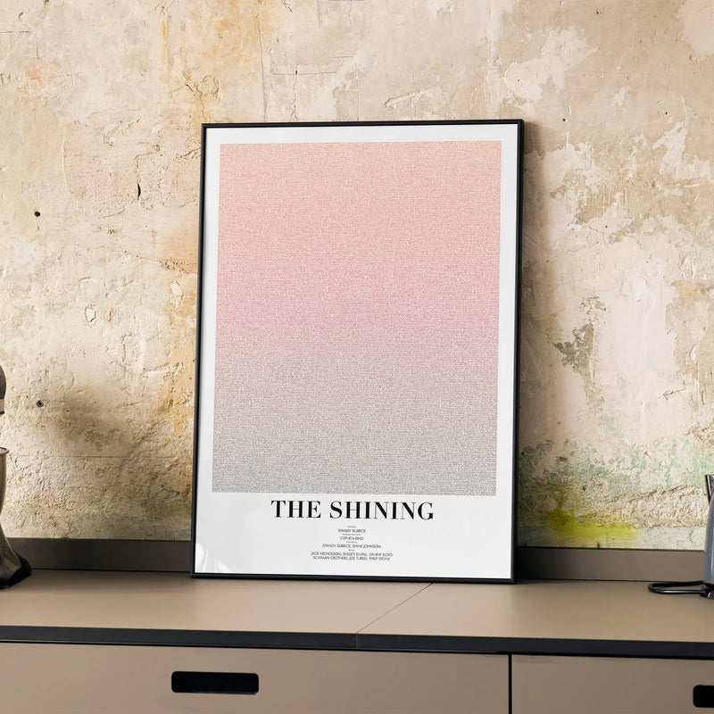 A framed The Shining movie script poster displayed on a cabinet in a minimalist interior.