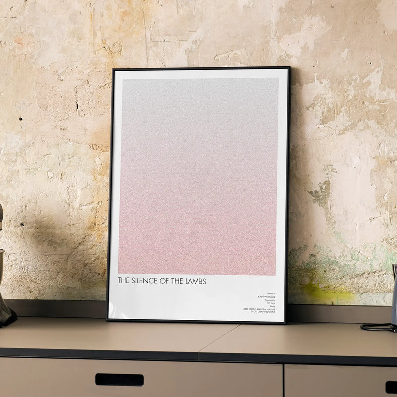 A framed The Silence of the Lambs movie script poster displayed on a cabinet in a minimalist interior.