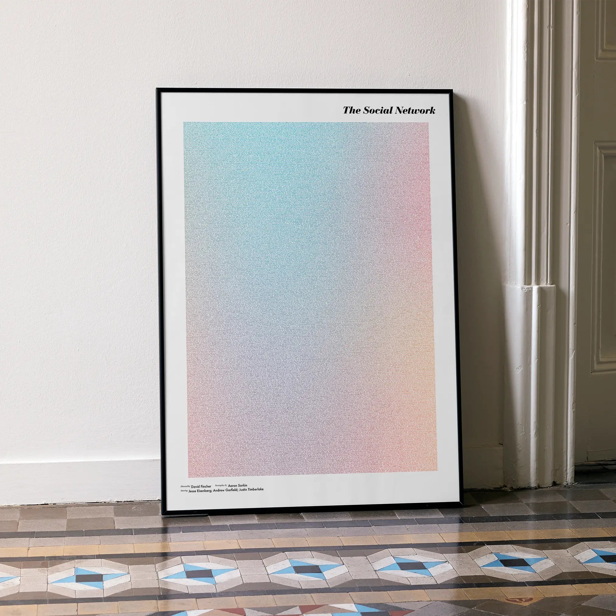 A framed The Social Network movie script poster leaning against a wall in a minimalist interior.