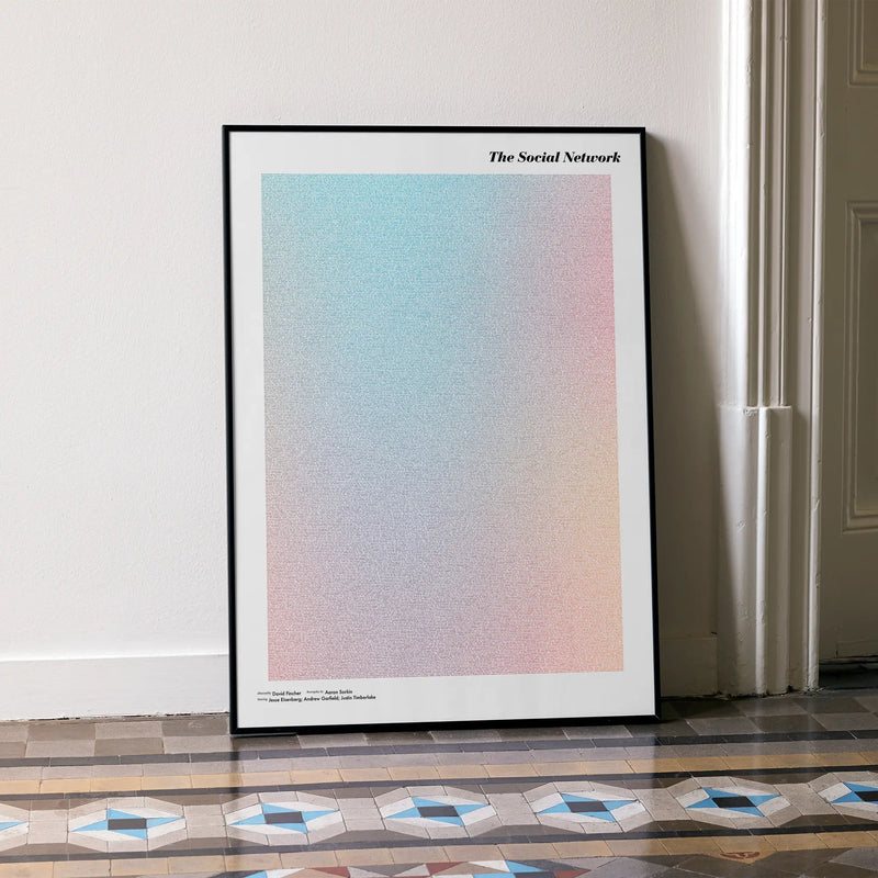 A framed The Social Network movie script poster leaning against a wall in a minimalist interior.
