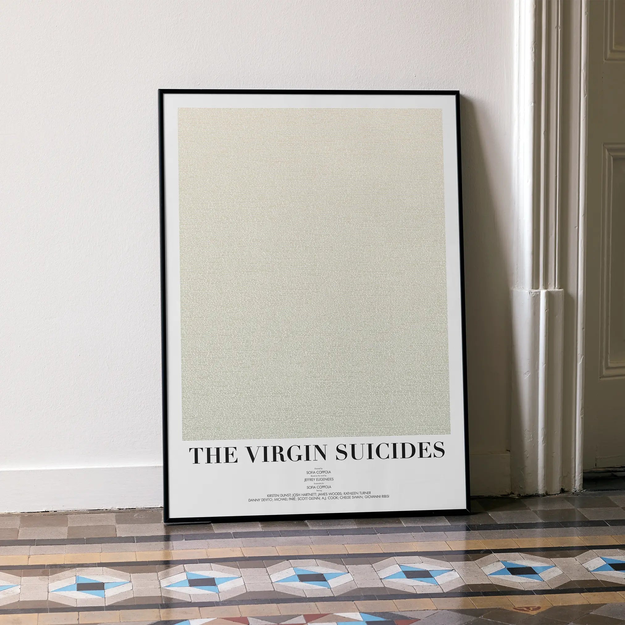 A framed The Virgin Suicides movie script poster leaning against a wall in a minimalist interior.