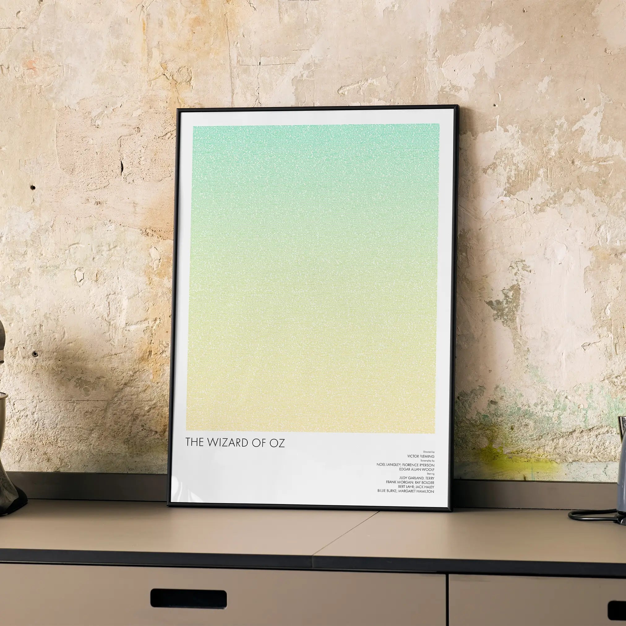 A framed The Wizard of Oz movie script poster displayed on a cabinet in a minimalist interior.