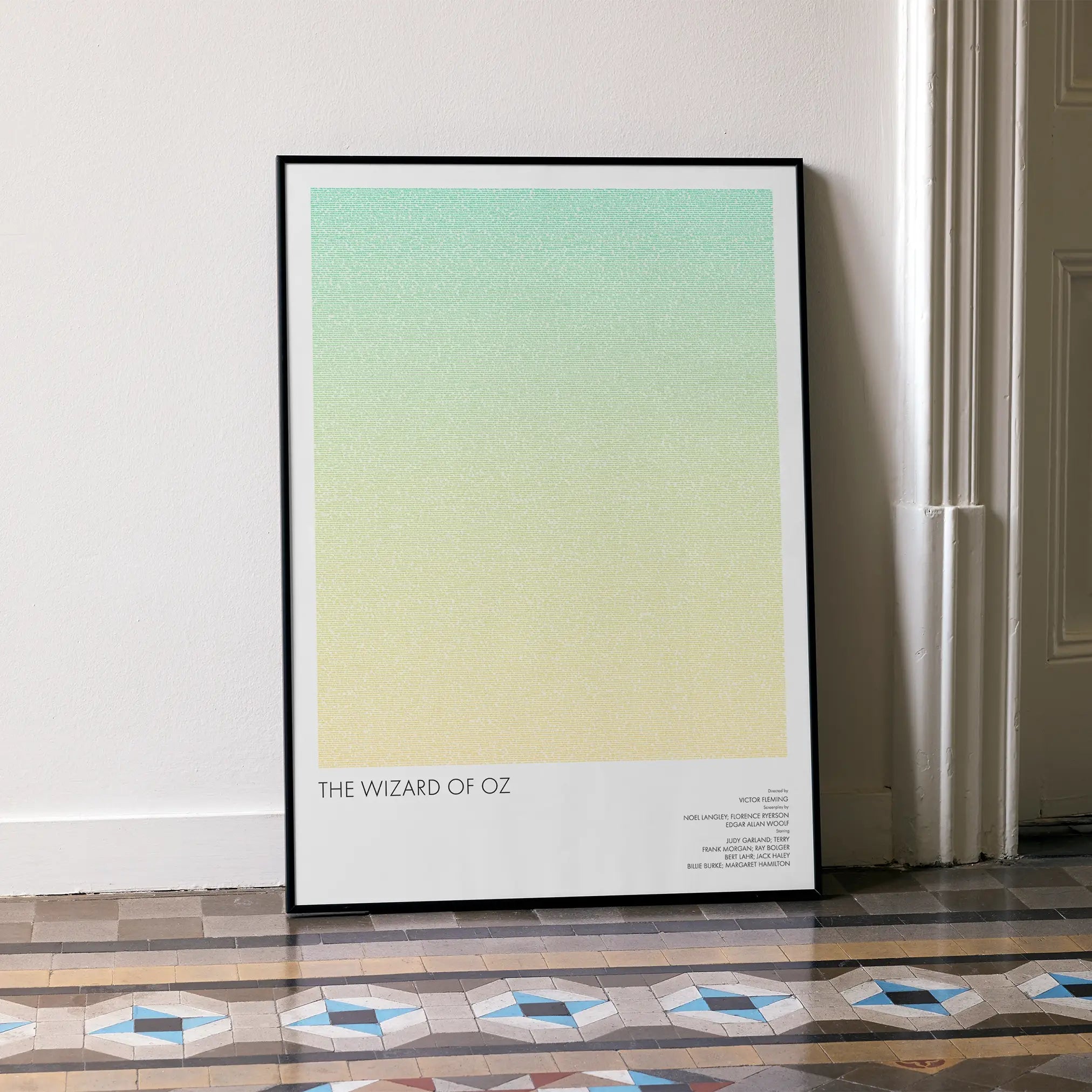 A framed The Wizard of Oz movie script poster leaning against a wall in a minimalist interior.
