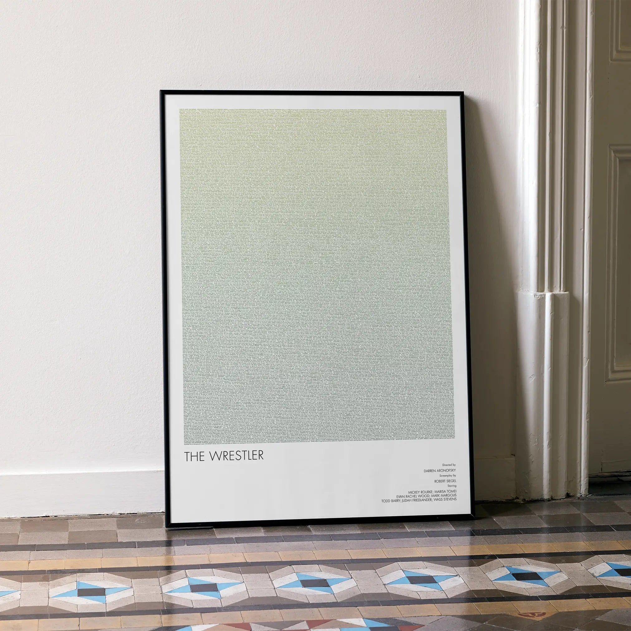 A framed The Wrestler movie script poster leaning against a wall in a minimalist interior.