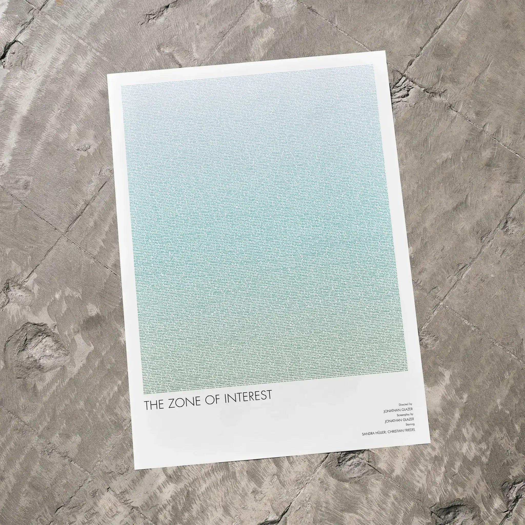 A The Zone of Interest movie script poster laid flat on a textured floor surface.