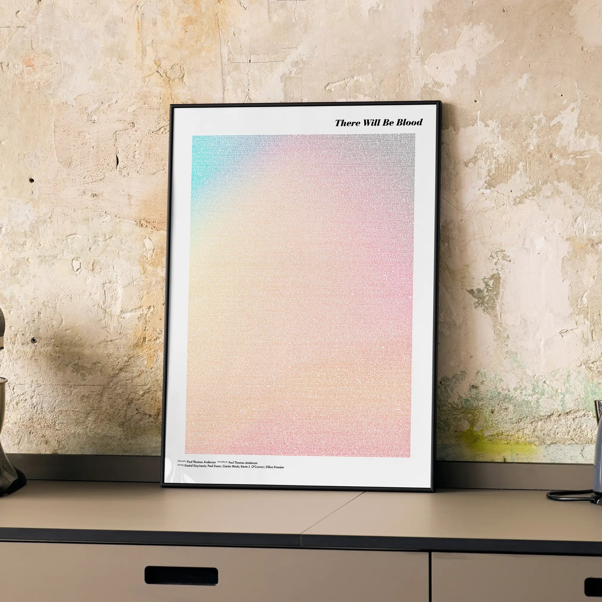 A framed There Will Be Blood movie script poster displayed on a cabinet in a minimalist interior.