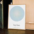 Framed poster with a circular design and 'Top Gun' text on a wooden surface.