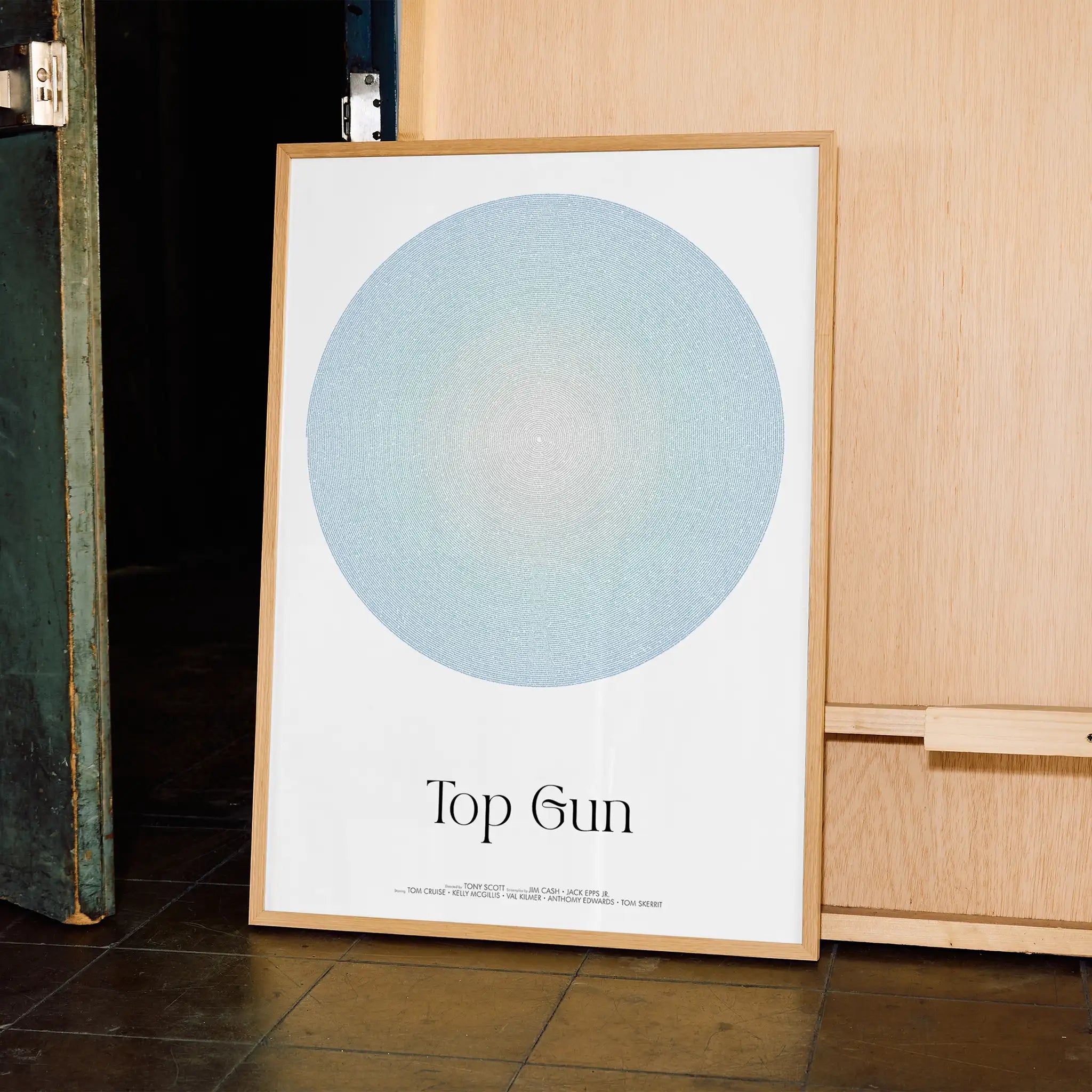 Framed poster with a circular design and 'Top Gun' text on a wooden surface.