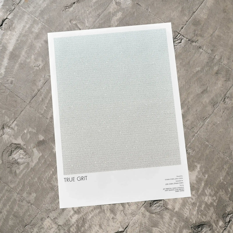 A True Grit movie script poster laid flat on a textured floor surface.