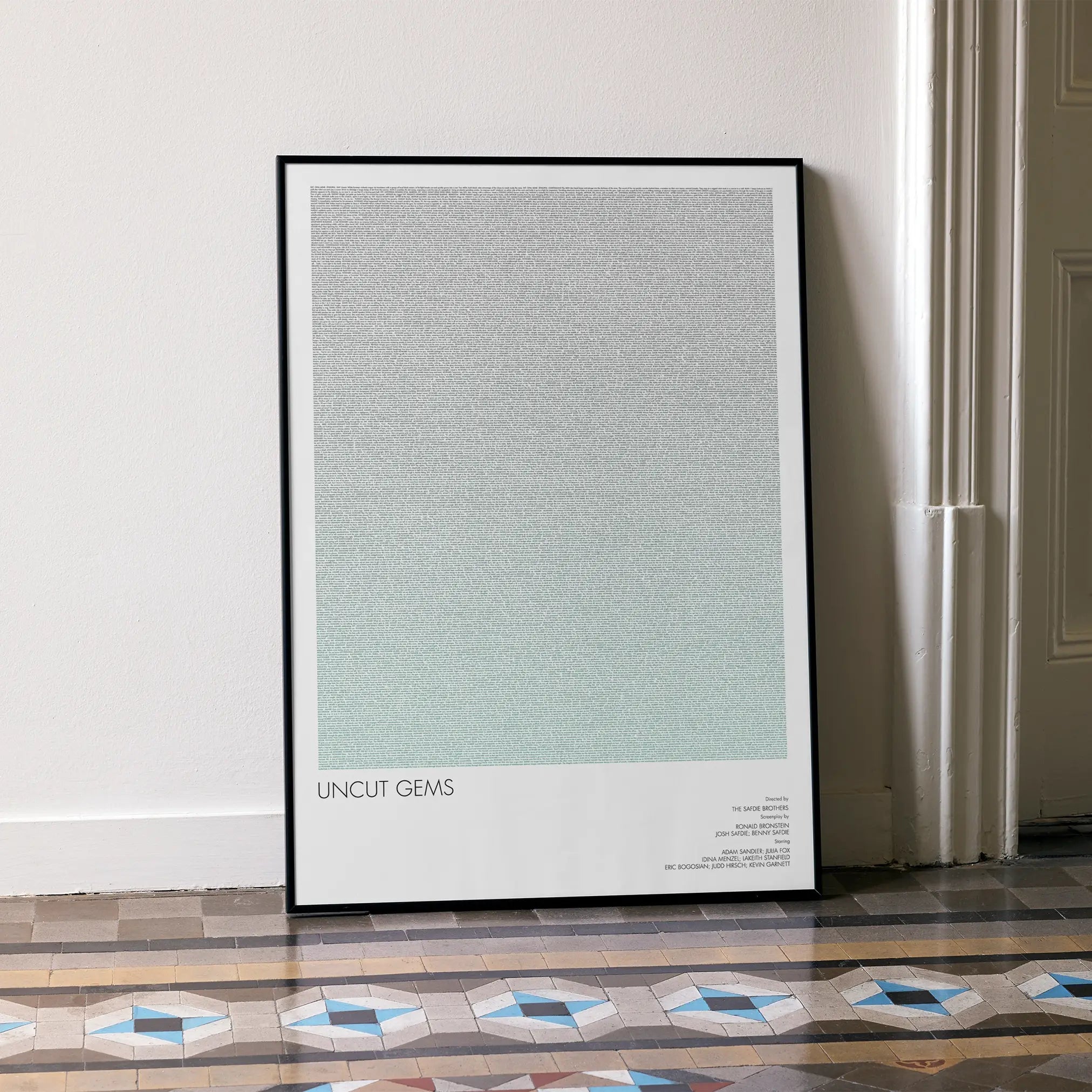 A framed Uncut Gems movie script poster leaning against a wall in a minimalist interior.