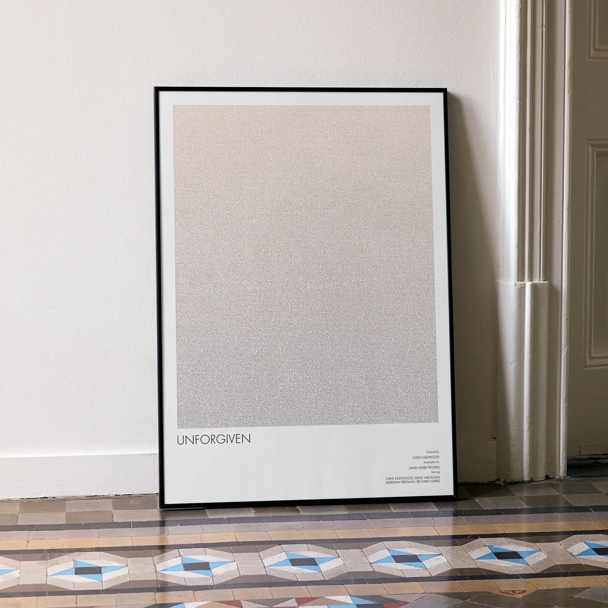 A framed Unforgiven movie script poster leaning against a wall in a minimalist interior.
