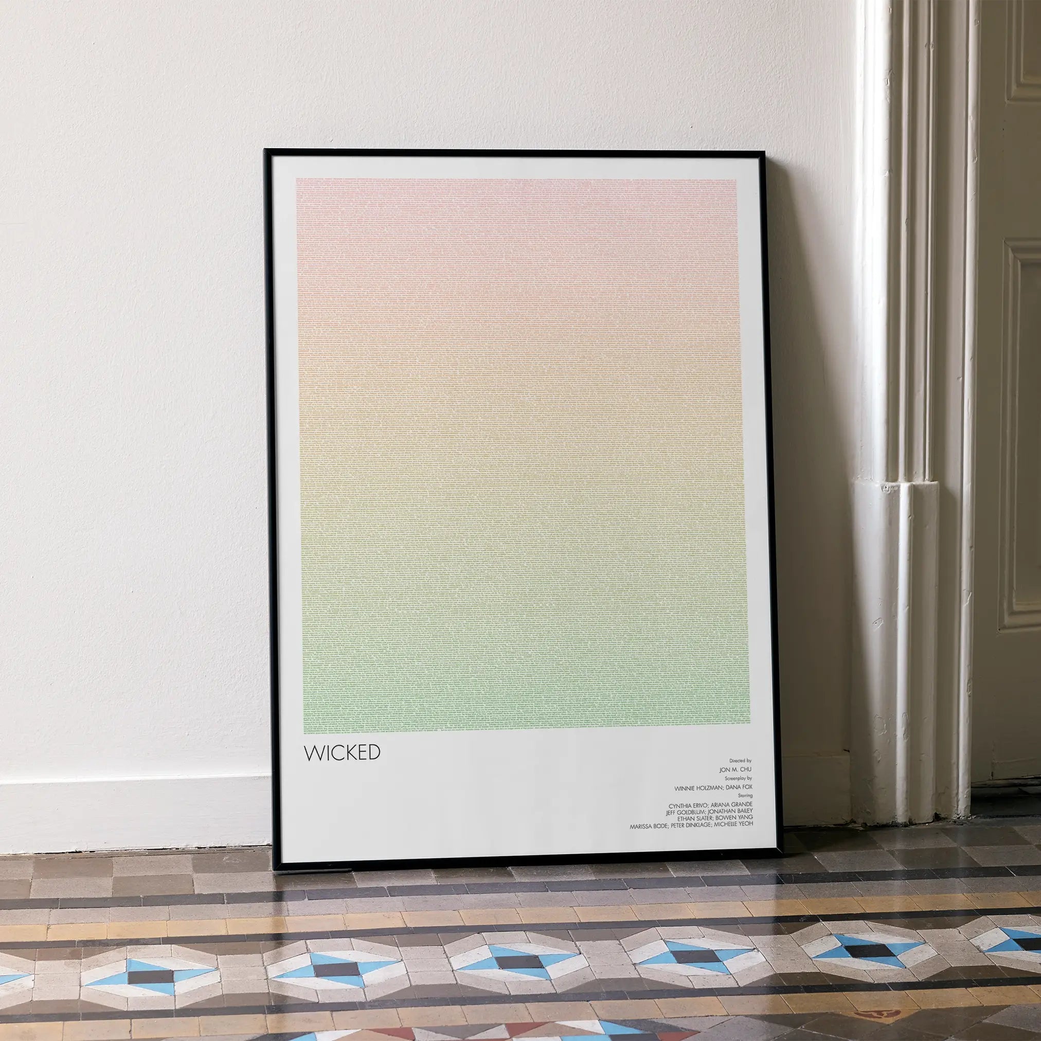 A framed Wicked movie script poster leaning against a wall in a minimalist interior.