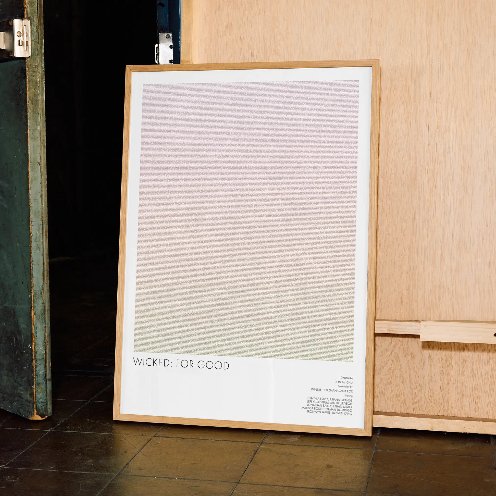 A framed Wicked For Good movie script poster leaning against a wall in a minimalist interior.