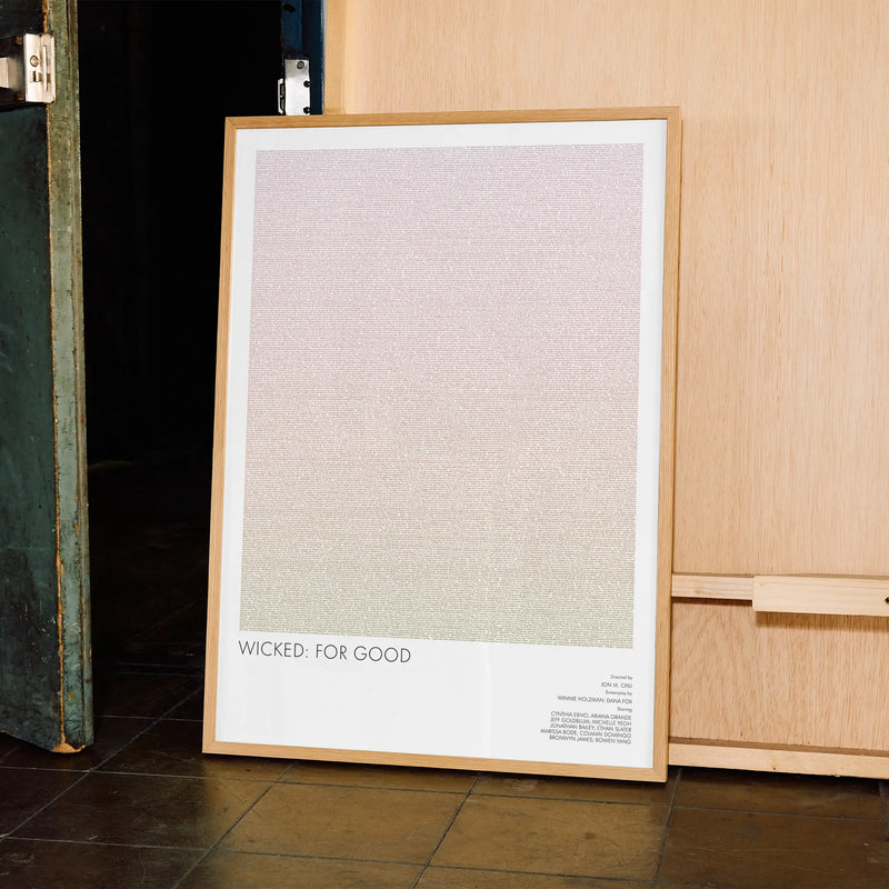 A framed Wicked For Good movie script poster leaning against a wall in a minimalist interior.